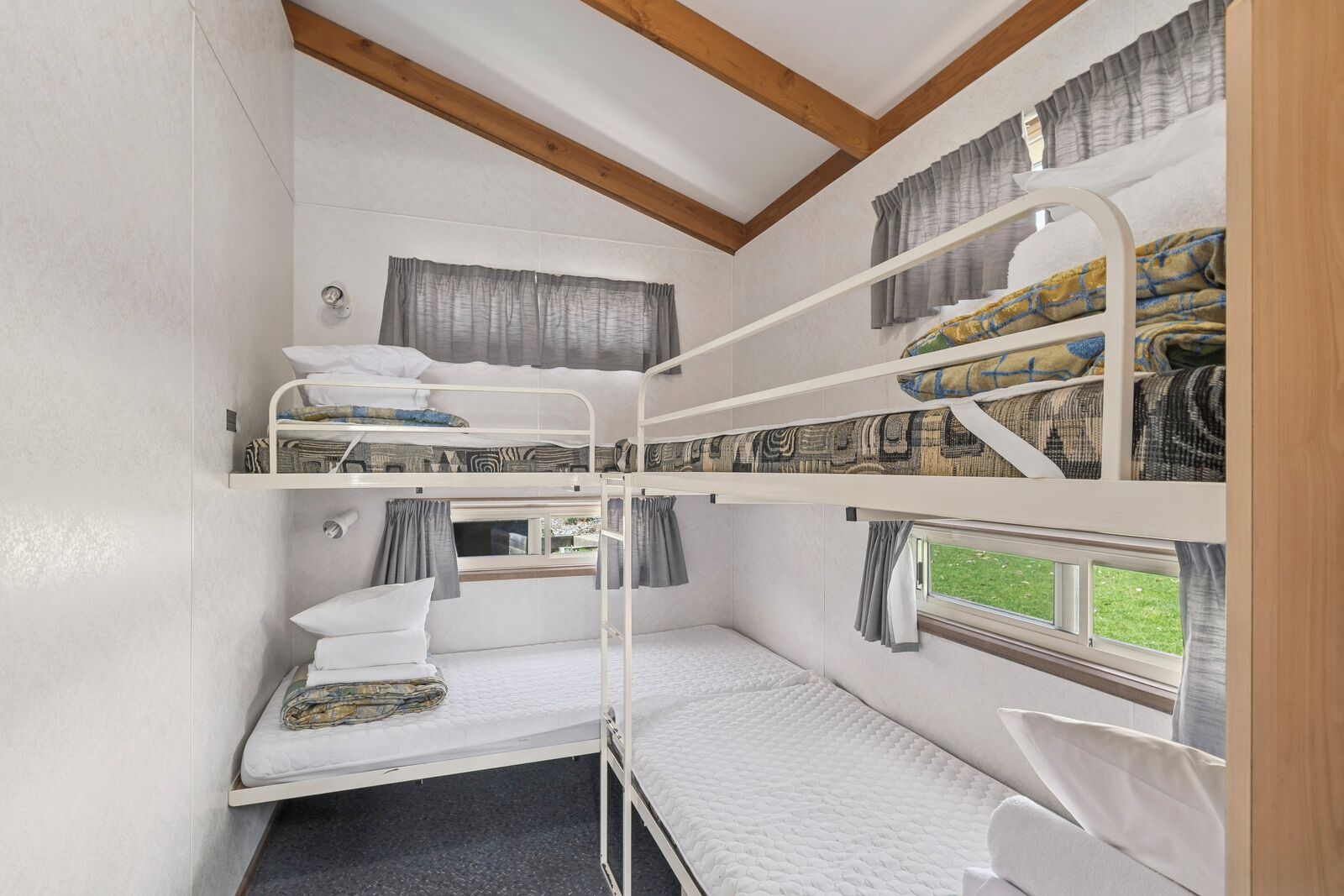 A compact, well-lit room with bunk beds, a window with curtains, and a small table with a lamp.