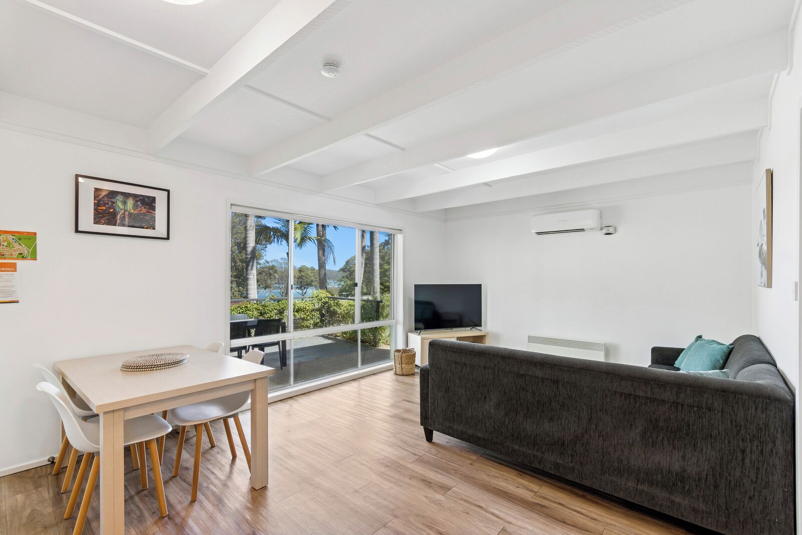 A modern living room with a grey sofa, a TV, and a dining area with a table and chairs.