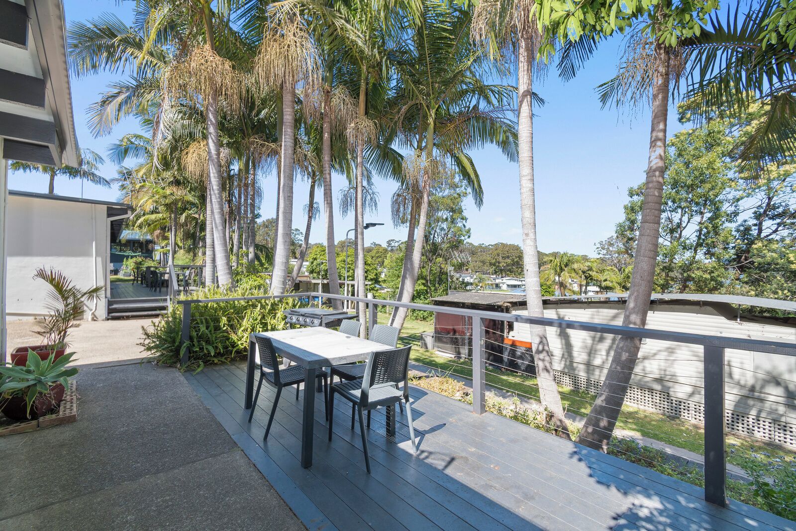 A deck with a table and chairs, surrounded by palm trees and a view of a residential area.