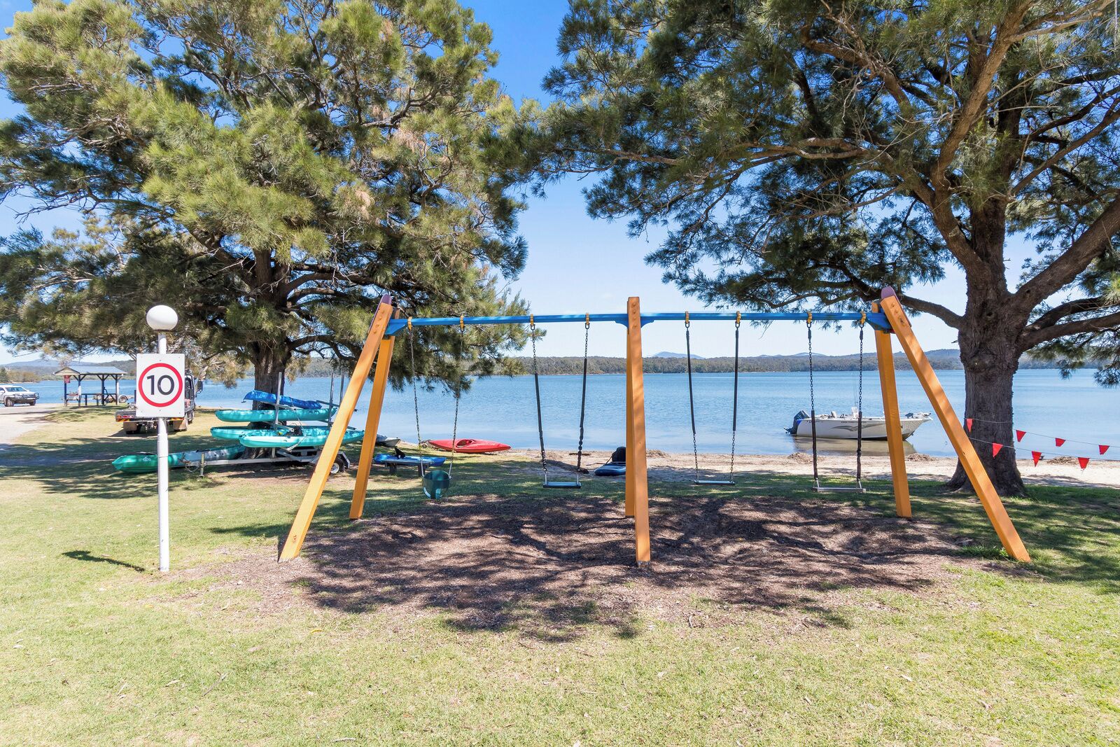 Un parque con columpios, una señal de límite de velocidad, botes y un lago.