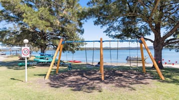 Un parque con columpios, una señal de límite de velocidad, botes y un lago.