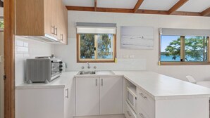 A modern kitchen with white cabinetry, a built-in oven, and a large window offering a view of the outdoors. - Ingenia Holidays Bermagui (Wallaga Lake)