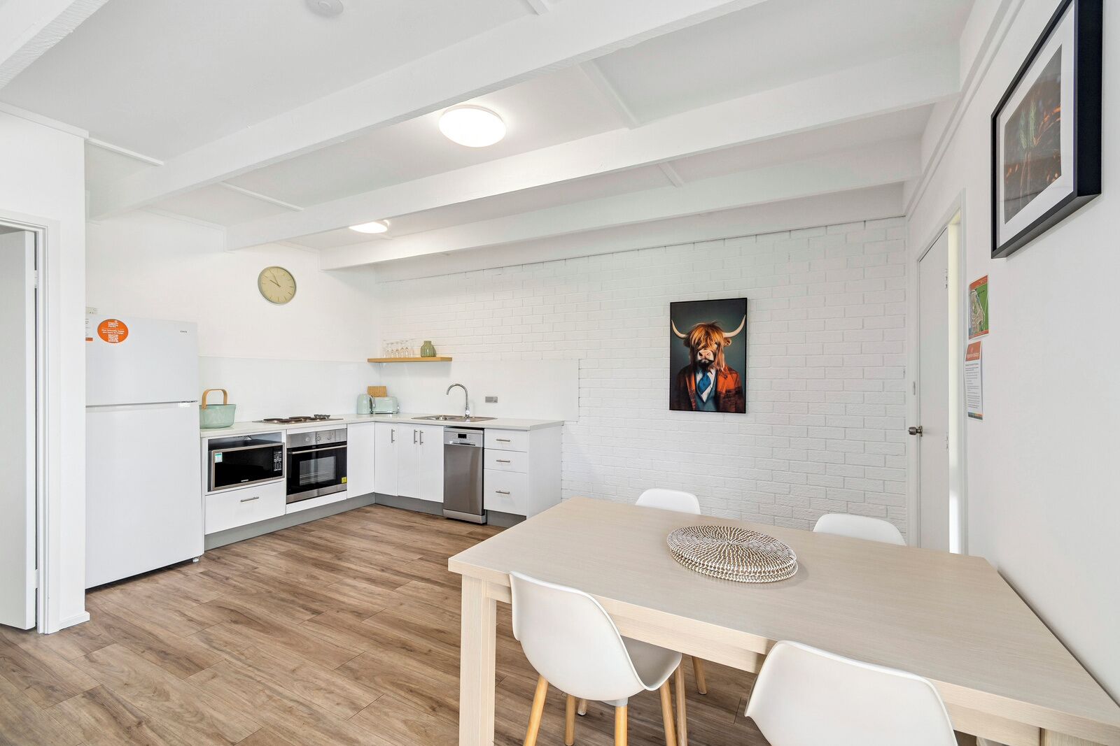 A modern kitchen with white cabinetry, a dining table with chairs, and a wall-mounted clock.