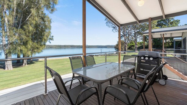 A covered outdoor area with a table and chairs, overlooking a lake and trees. - Ingenia Holidays Bermagui (Wallaga Lake)