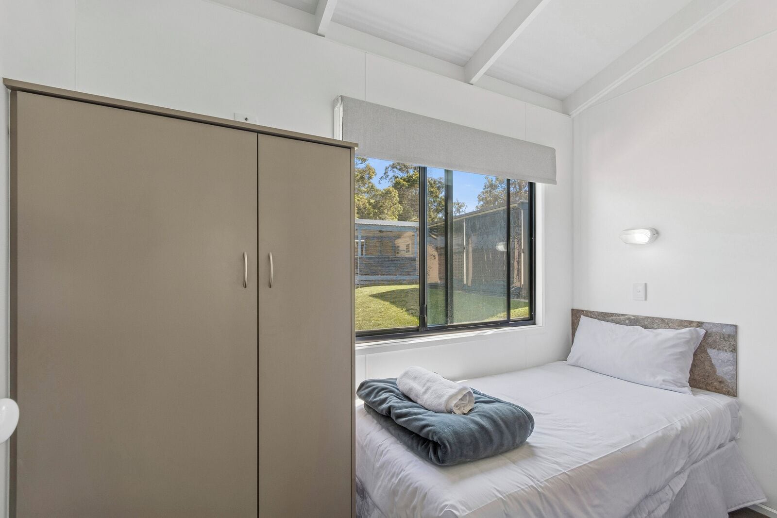 Ein Schlafzimmer mit Bett, Kleiderschrank, Fenster und Blick nach draußen.