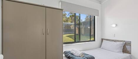 Ein Schlafzimmer mit Bett, Kleiderschrank, Fenster und Blick nach draußen.