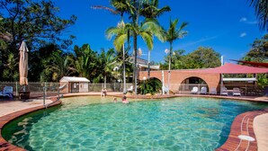 A swimming pool with clear water, surrounded by palm trees and a brick building. - Ingenia Holidays South West Rocks (South West Rocks)