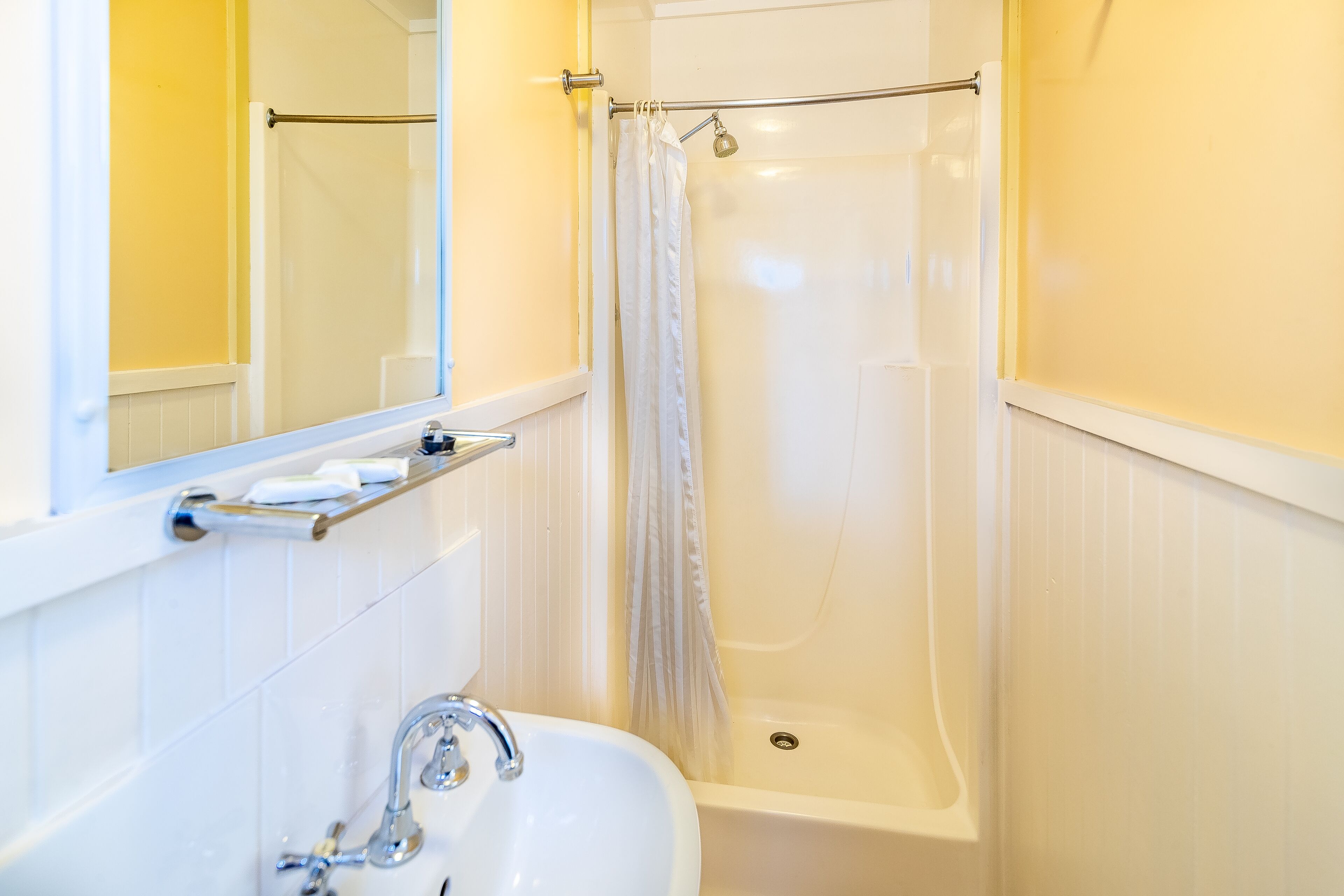 A bathroom with a white sink, a mirror, a shower with a curtain, and a towel rack.