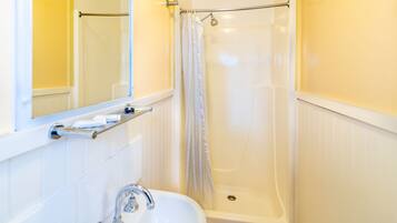 A bathroom with a white sink, a mirror, a shower with a curtain, and a towel rack.
