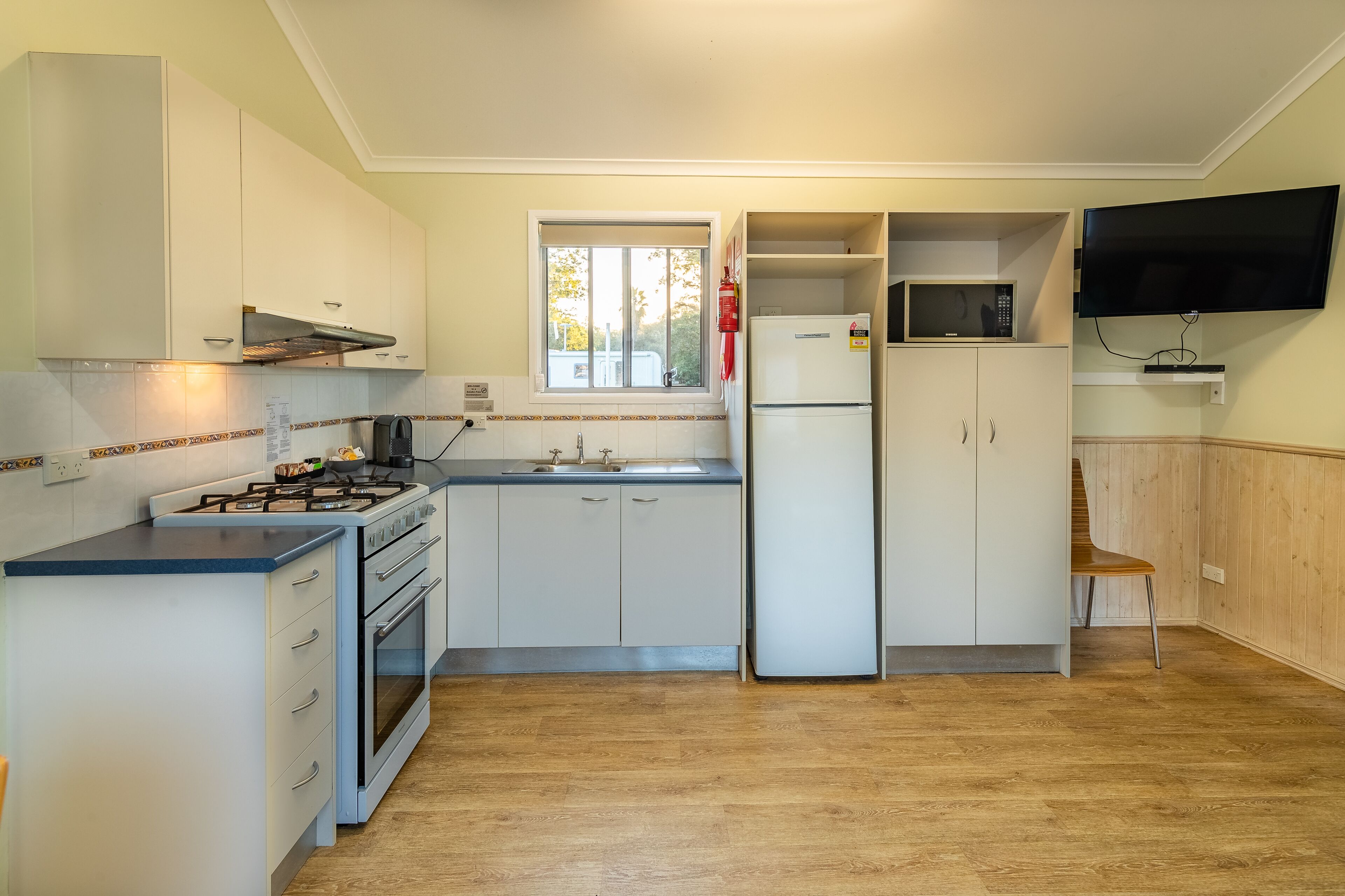 A compact kitchen with white cabinets, a gas stove, a microwave, and a TV mounted on the wall.