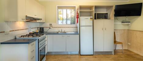 A compact kitchen with white cabinets, a gas stove, a microwave, and a TV mounted on the wall.