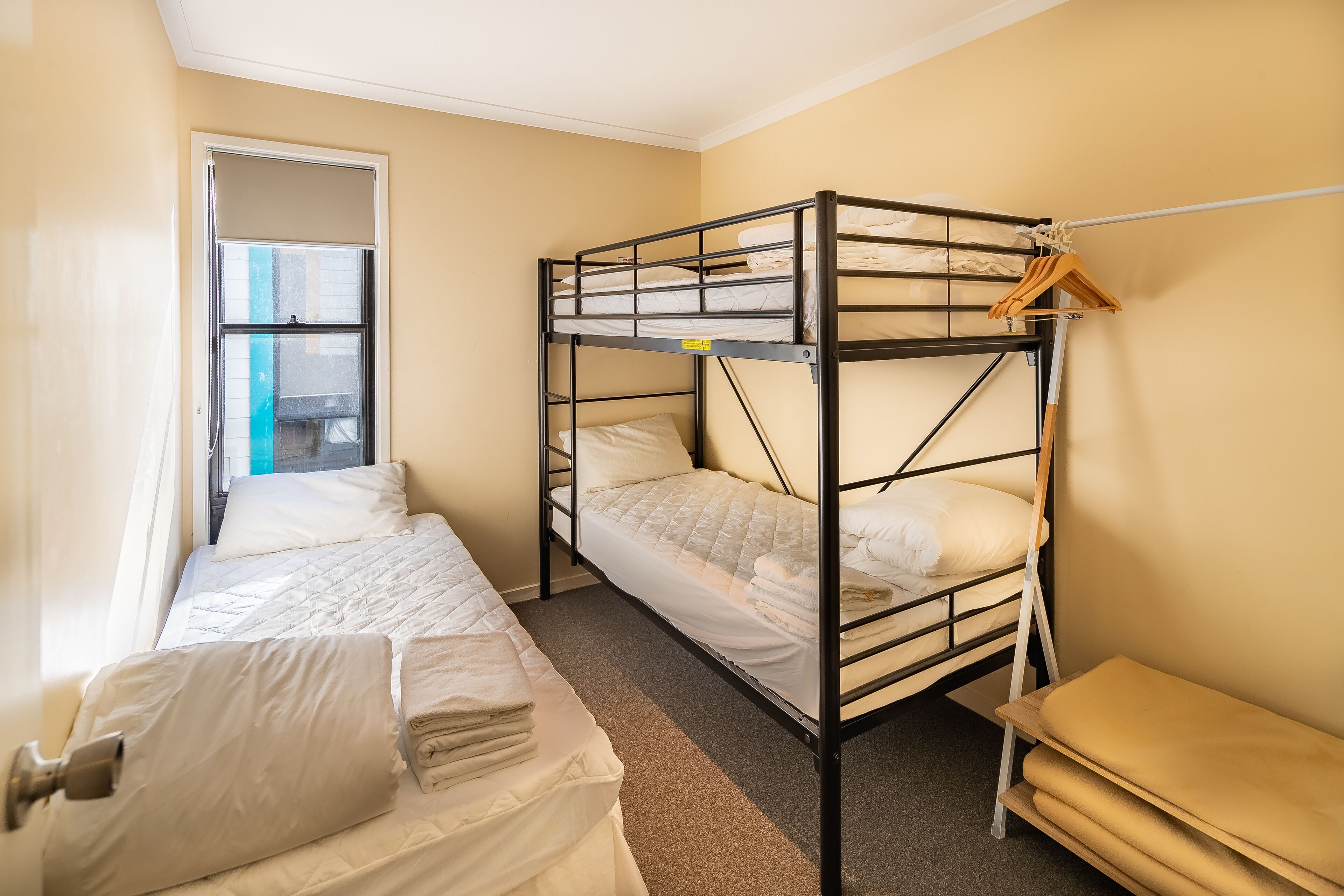 A dorm-style room with bunk beds, a small bench, and a window.