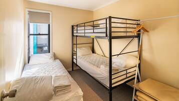 A dorm-style room with bunk beds, a small bench, and a window.