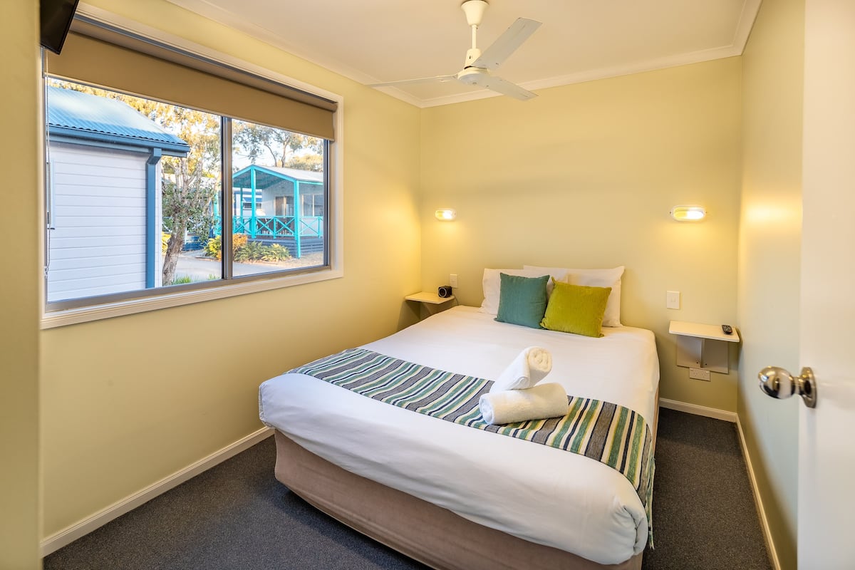 A hotel room with a bed, a window, a ceiling fan, and a nightstand.