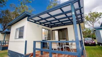 A mobile home with a covered porch, a dining area with chairs, and a car parked outside.