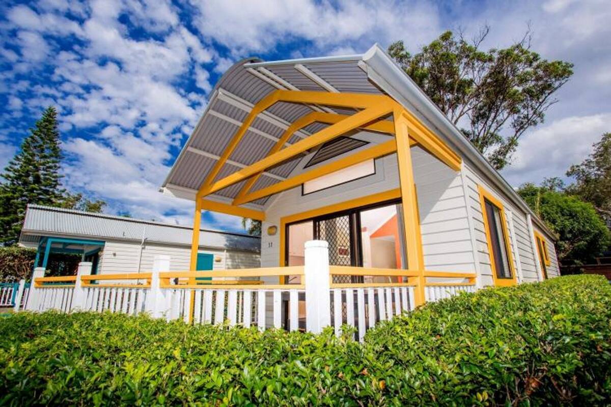 A modern house with a white exterior and yellow accents, featuring a covered porch and a fenced yard.