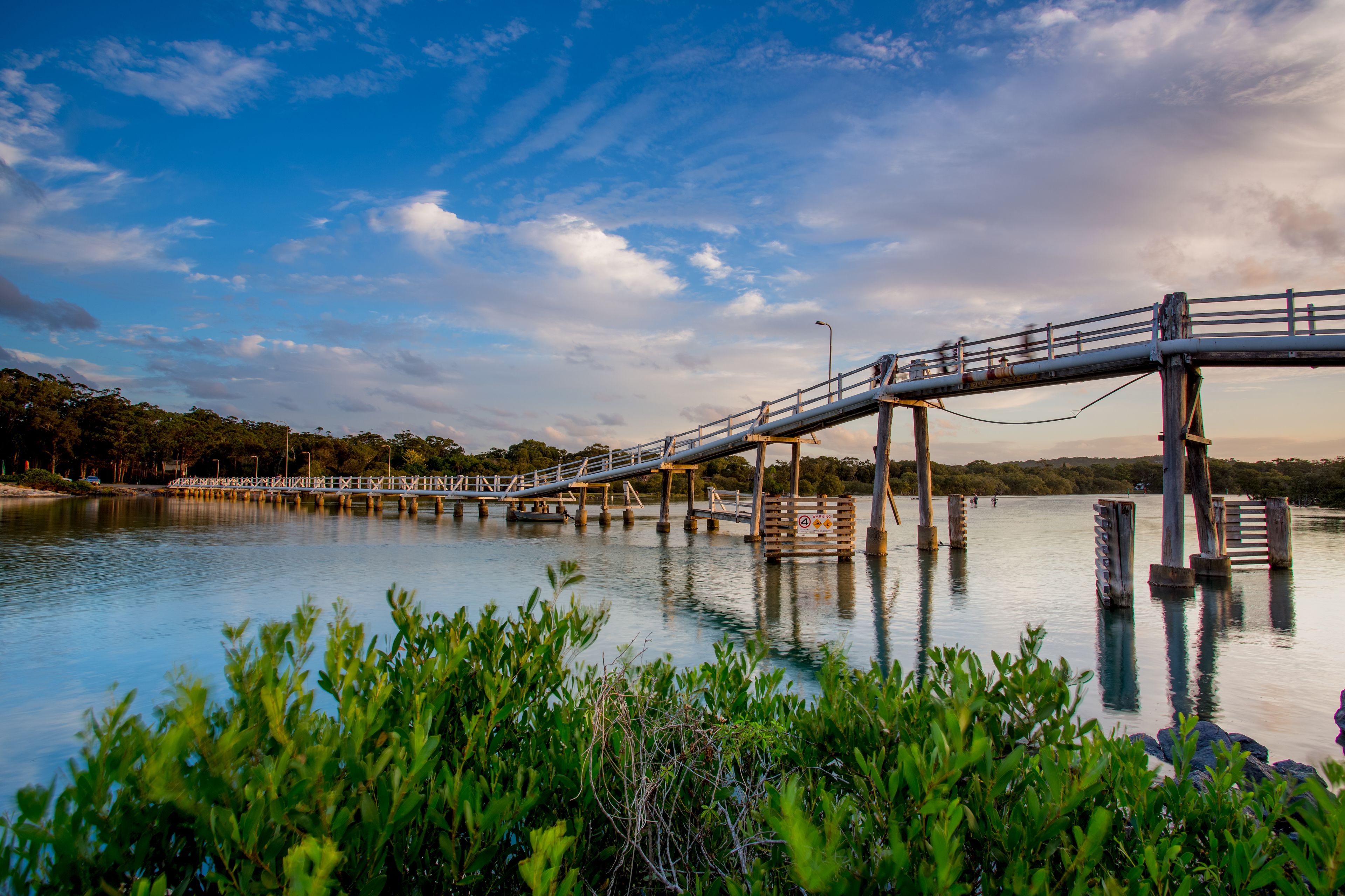 A bridge over a calm body of water with greenery in the foreground.