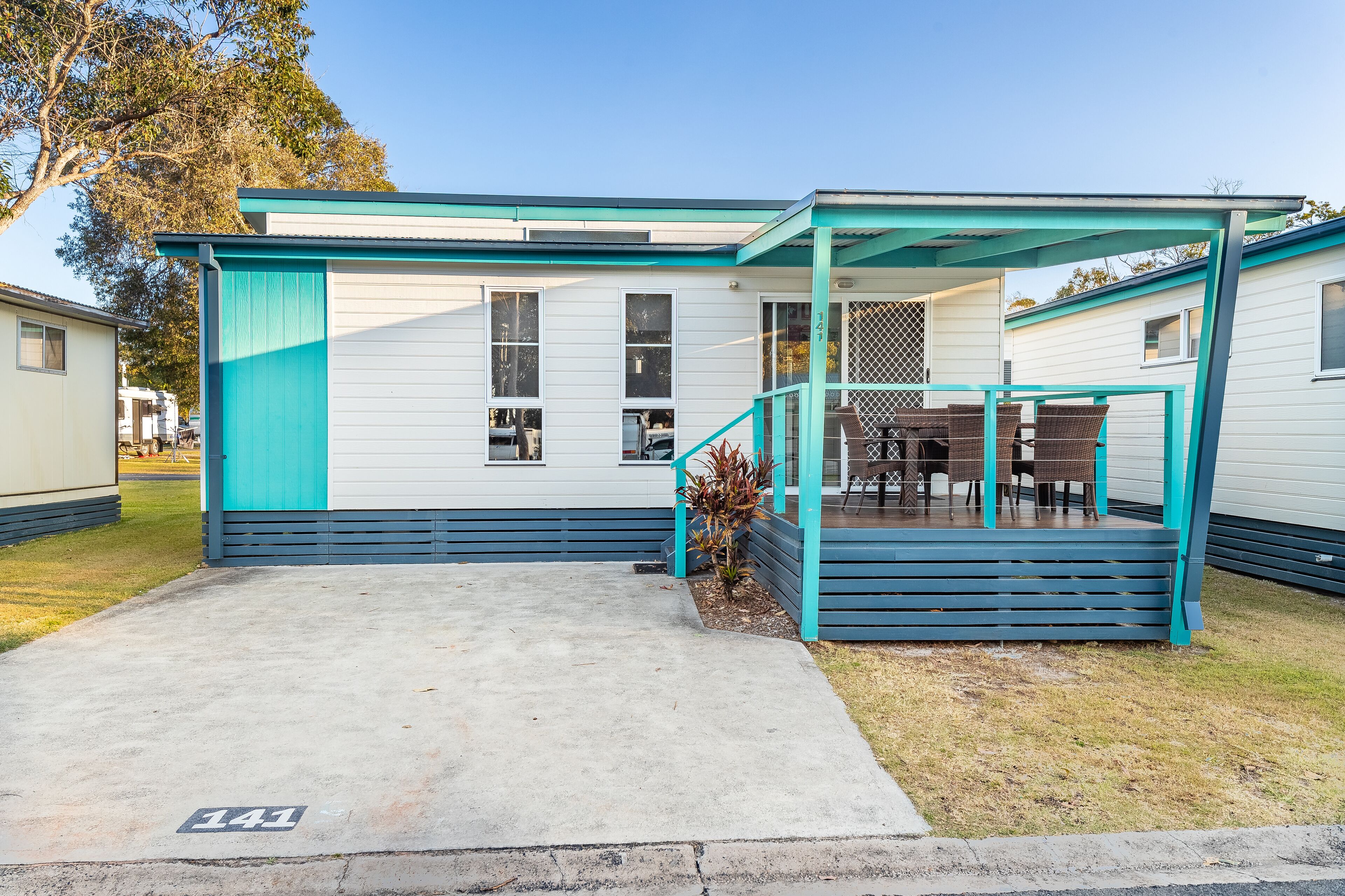 A single-story mobile home with a covered porch and a concrete driveway marked with the number 141.