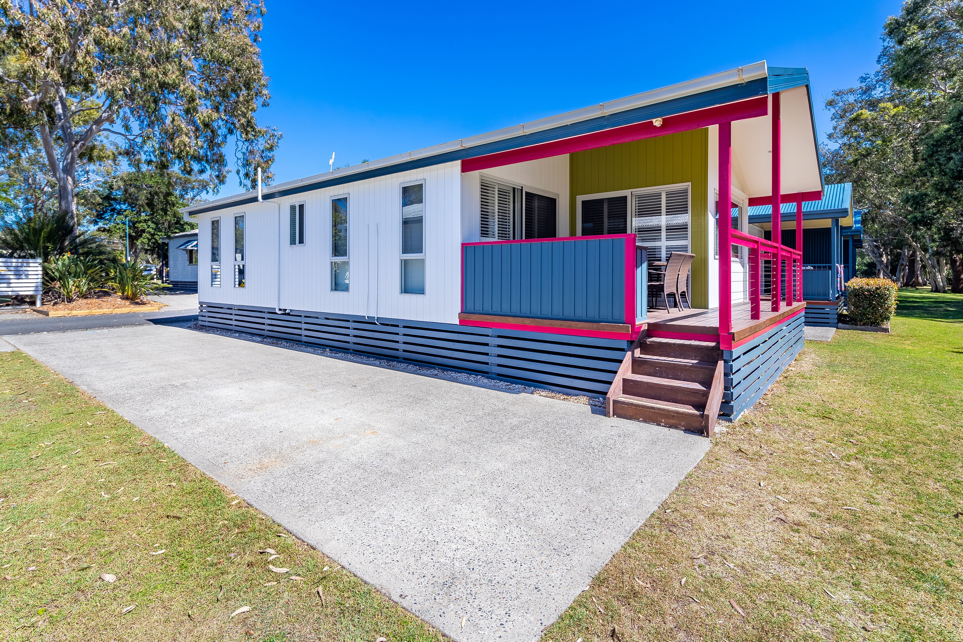 A single-story mobile home with a porch, a concrete driveway, and a grassy yard.
