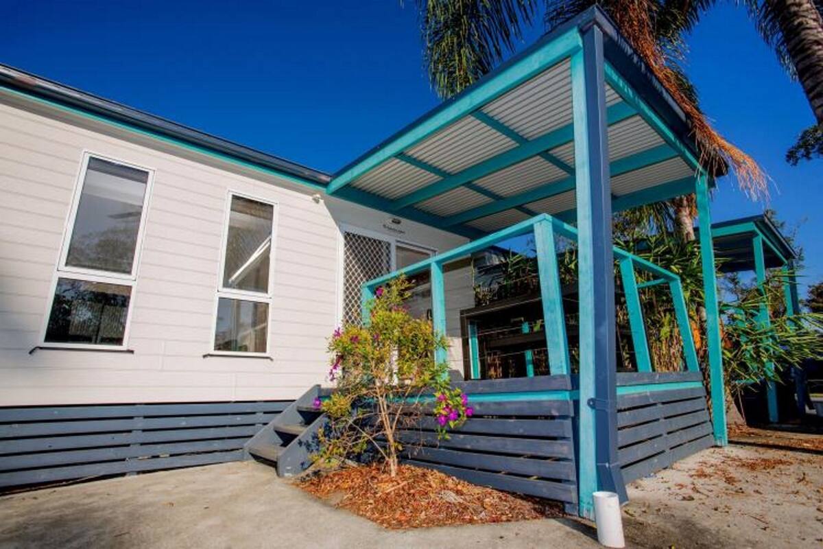 A white mobile home with a blue porch and a small tree with purple flowers.