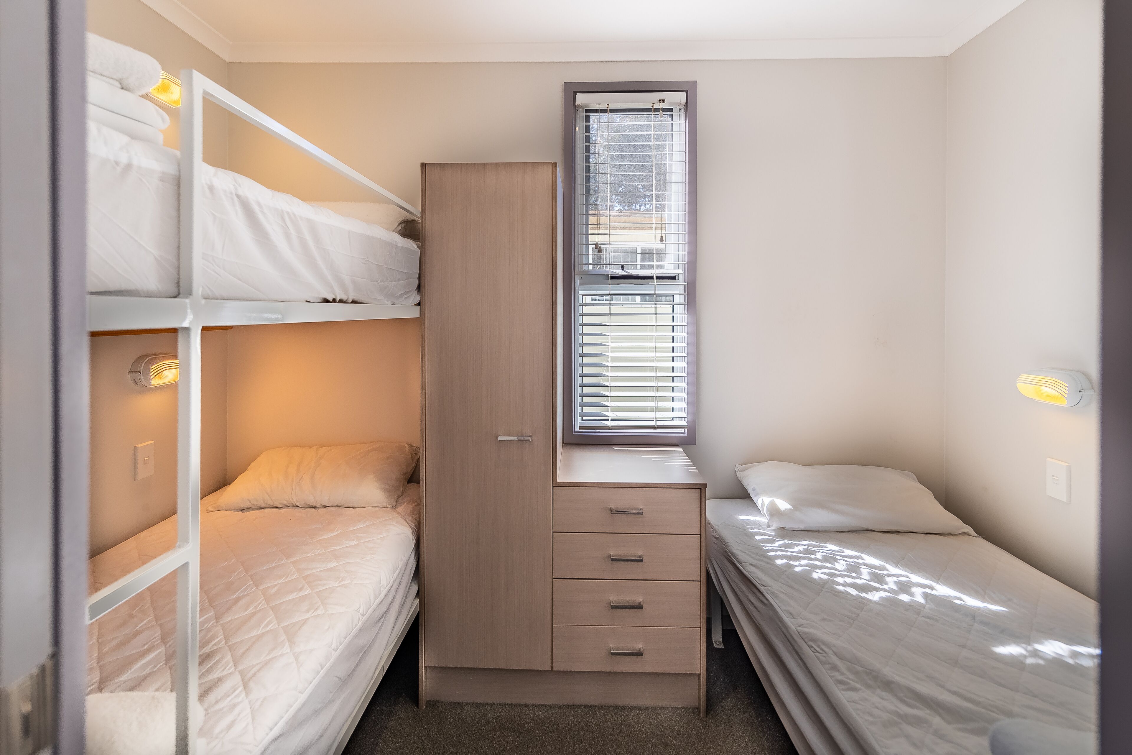 A compact room with bunk beds, a wardrobe, and a window with blinds.