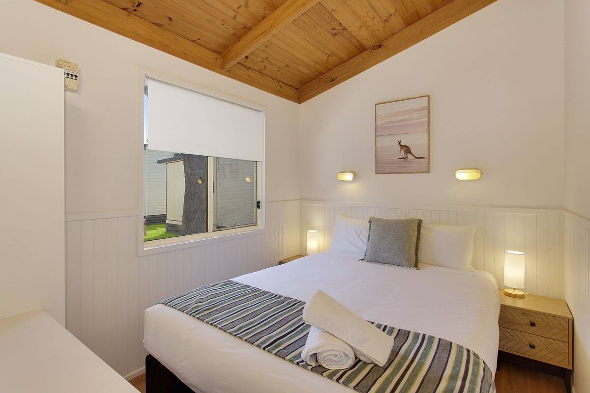 A bedroom with a bed, bedside lamps, a window with a view, and a painting on the wall.