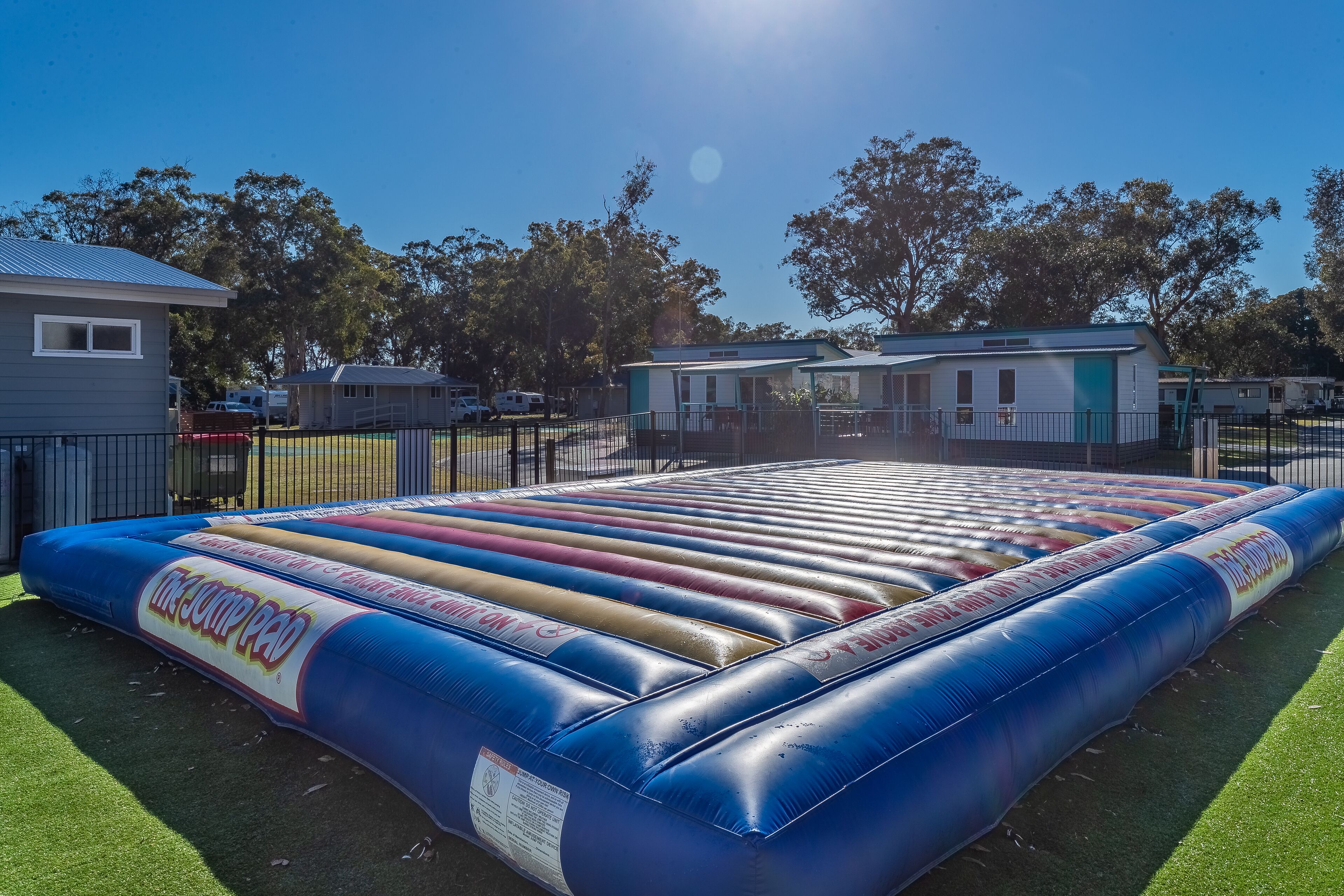 An inflatable jump pad in a fenced outdoor area with a clear sky.