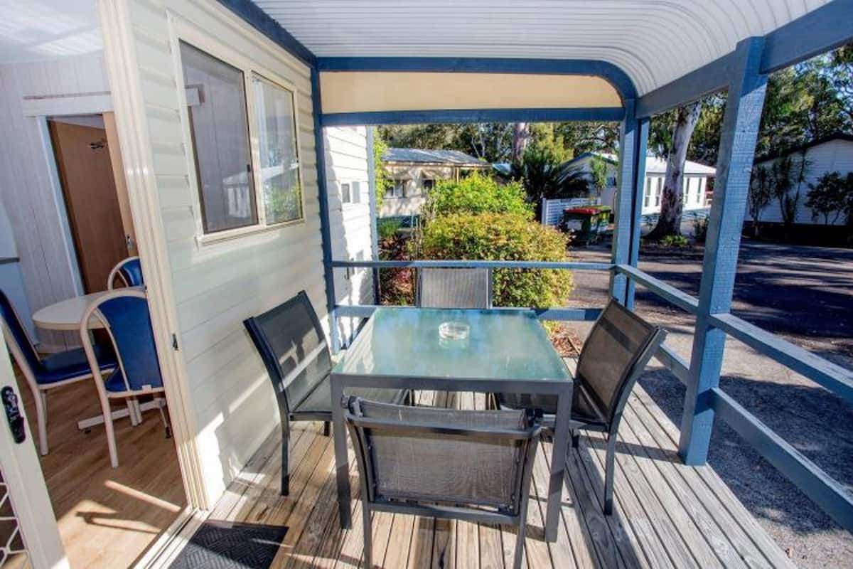 A covered outdoor patio with a table and chairs, a door, and a view of the neighborhood.