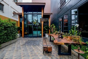 Un patio al aire libre con suelo de baldosas, una mesa de madera con plantas en macetas y un gato sentado sobre la mesa.