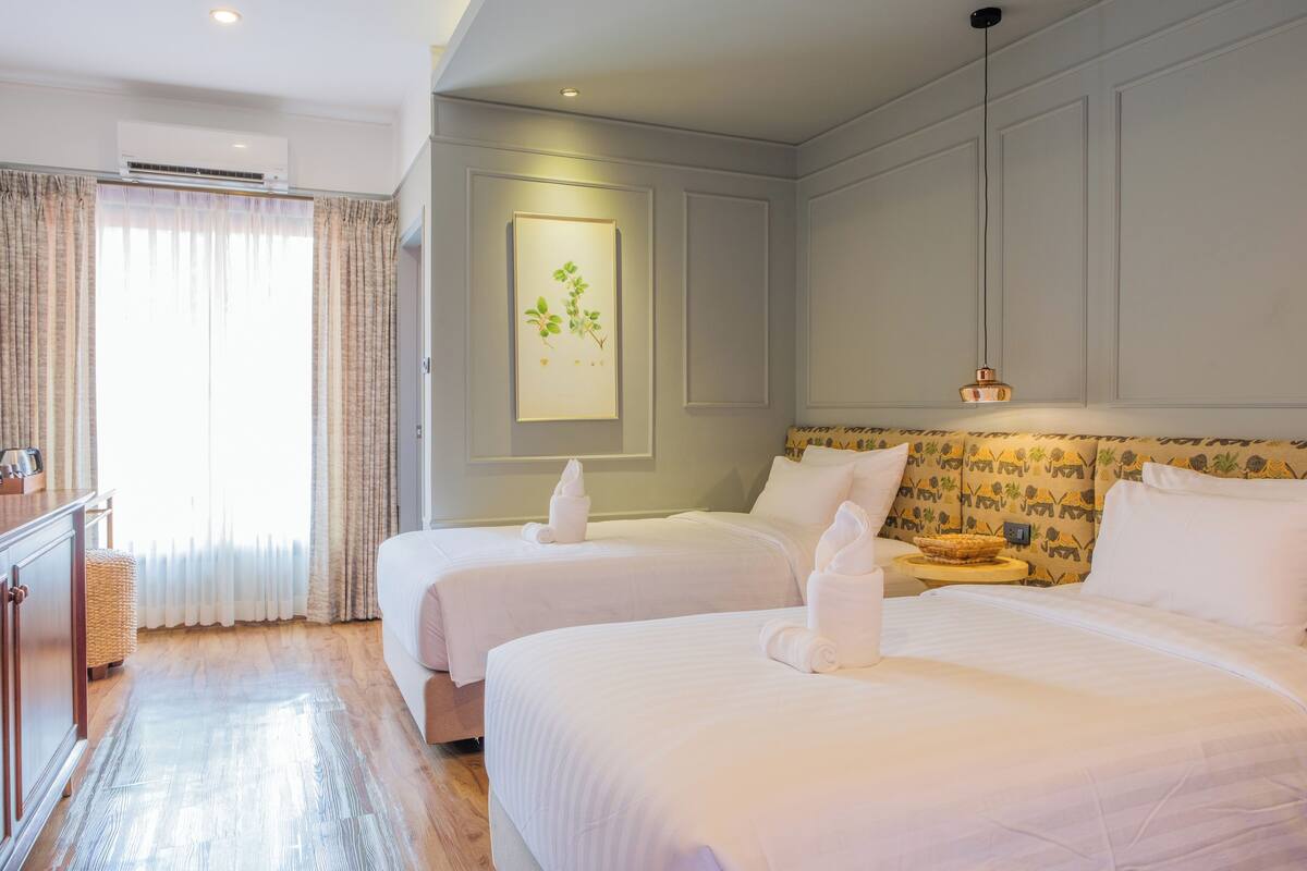 A hotel room with two beds, a bedside table, a lamp, and a framed picture on the wall.