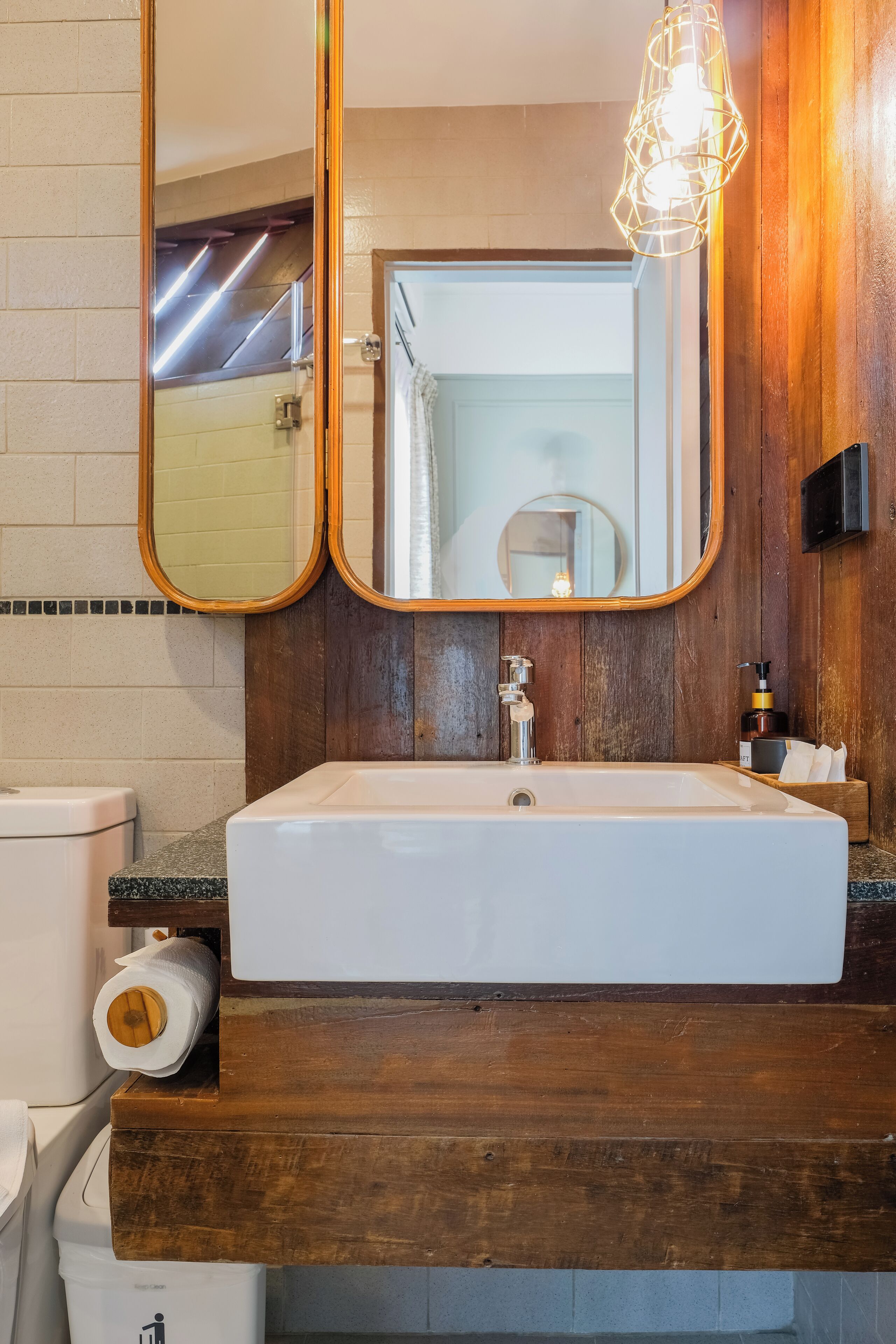 A bathroom with a wooden vanity, a white sink, a mirror, and a towel dispenser.