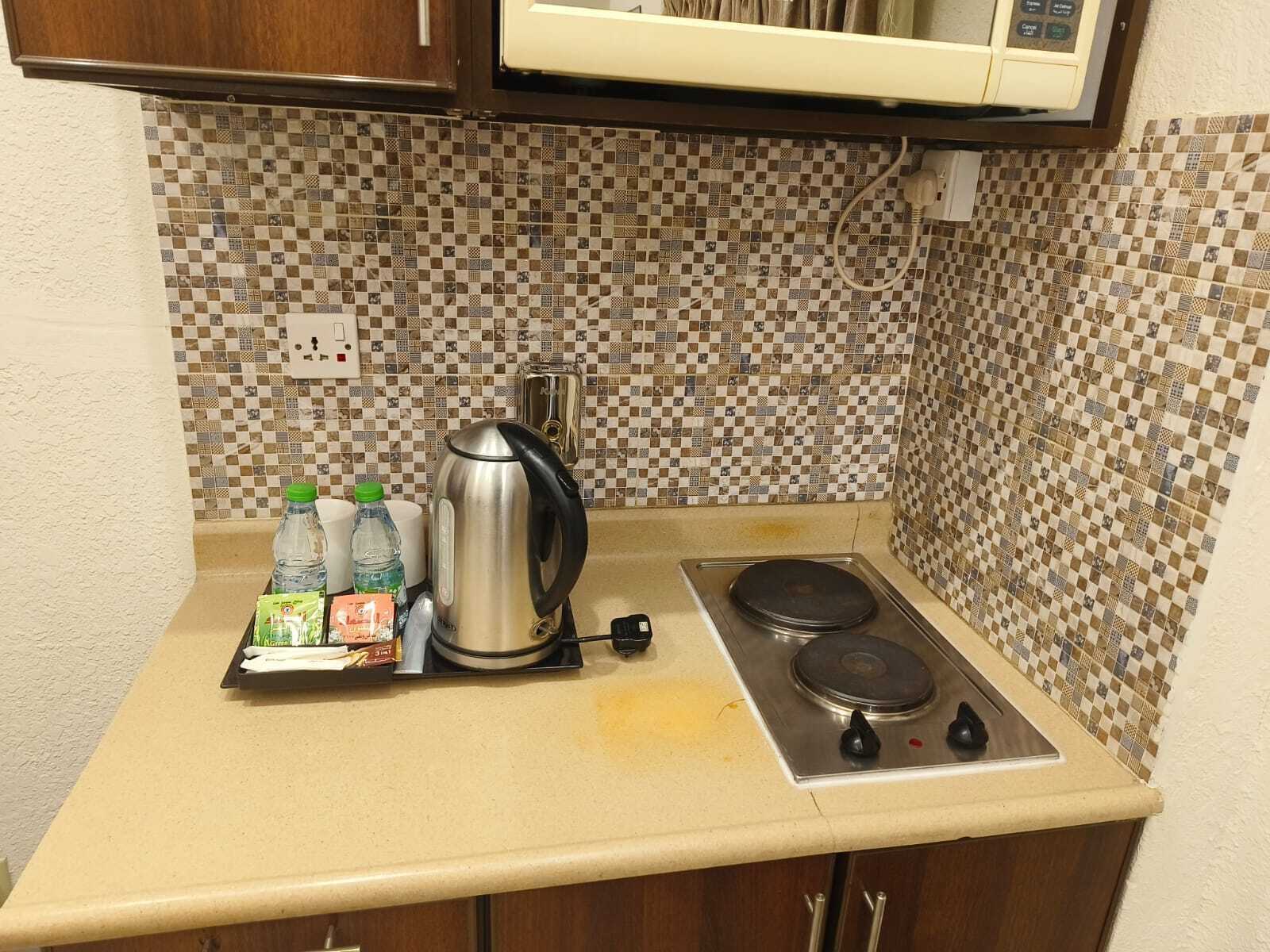 A kitchenette with a checkered backsplash, a stainless steel kettle, a toaster, and a small tray with bottled water and snacks.