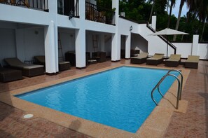 A swimming pool with lounge chairs and umbrellas, surrounded by a white building with multiple balconies.