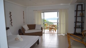 Habitación de hotel con cama, sofá, mesa de comedor con sillas y balcón con vistas.