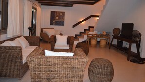 Una sala de estar con muebles de mimbre, una escalera y un televisor sobre un soporte de madera.