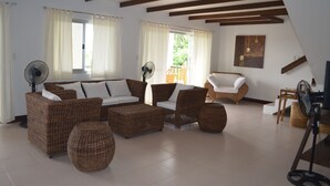 Amplia sala de estar con mobiliario de mimbre, un sofá grande y un ventilador.