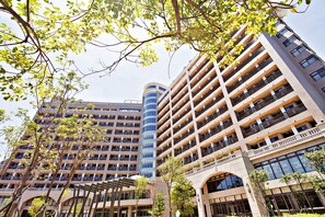 Un aparcamiento de varios pisos con diseño moderno, rodeado de árboles y un edificio con fachada de vidrio curvo.