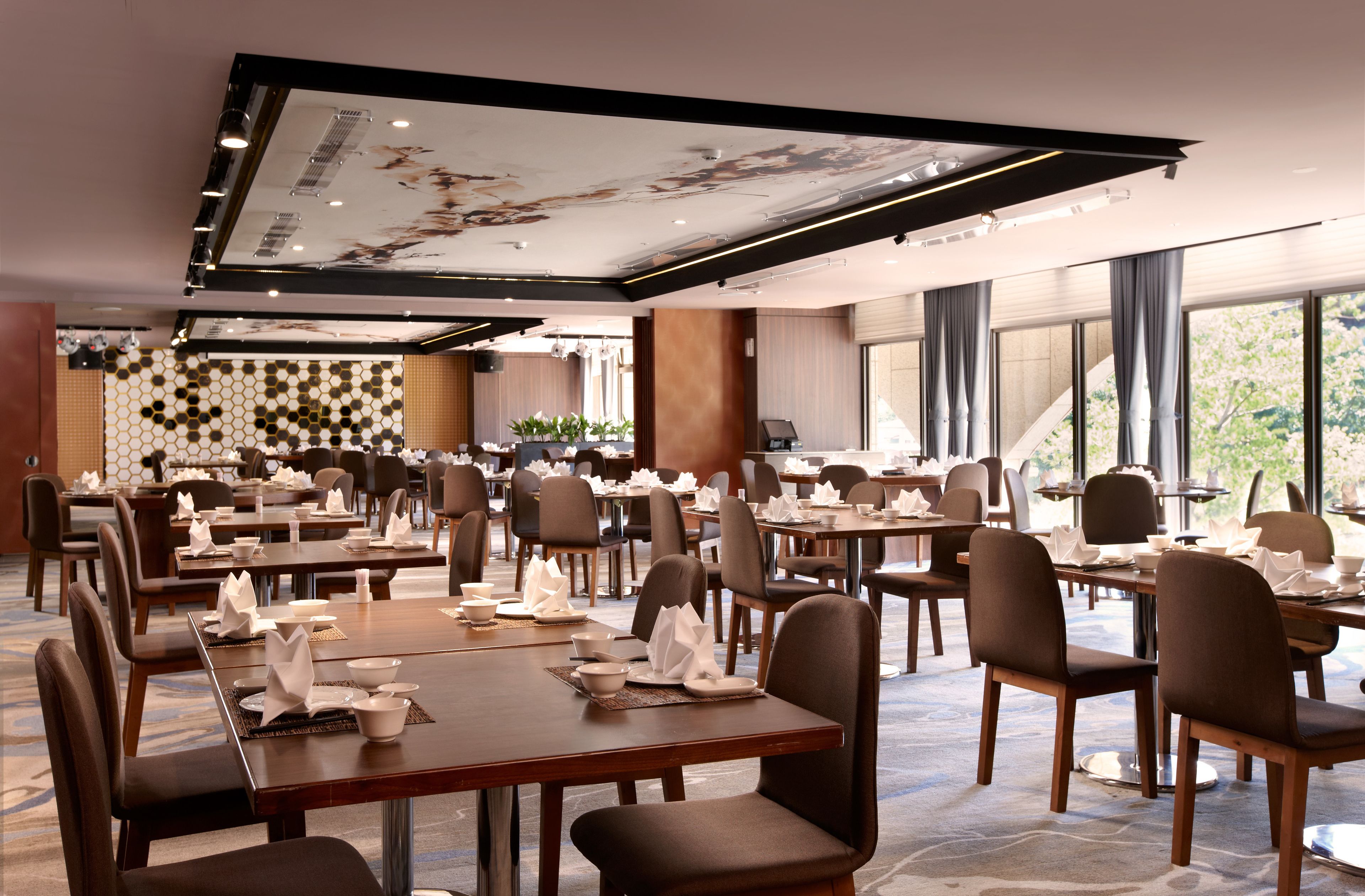 A spacious dining area with multiple tables and chairs, large windows, and a modern ceiling design.