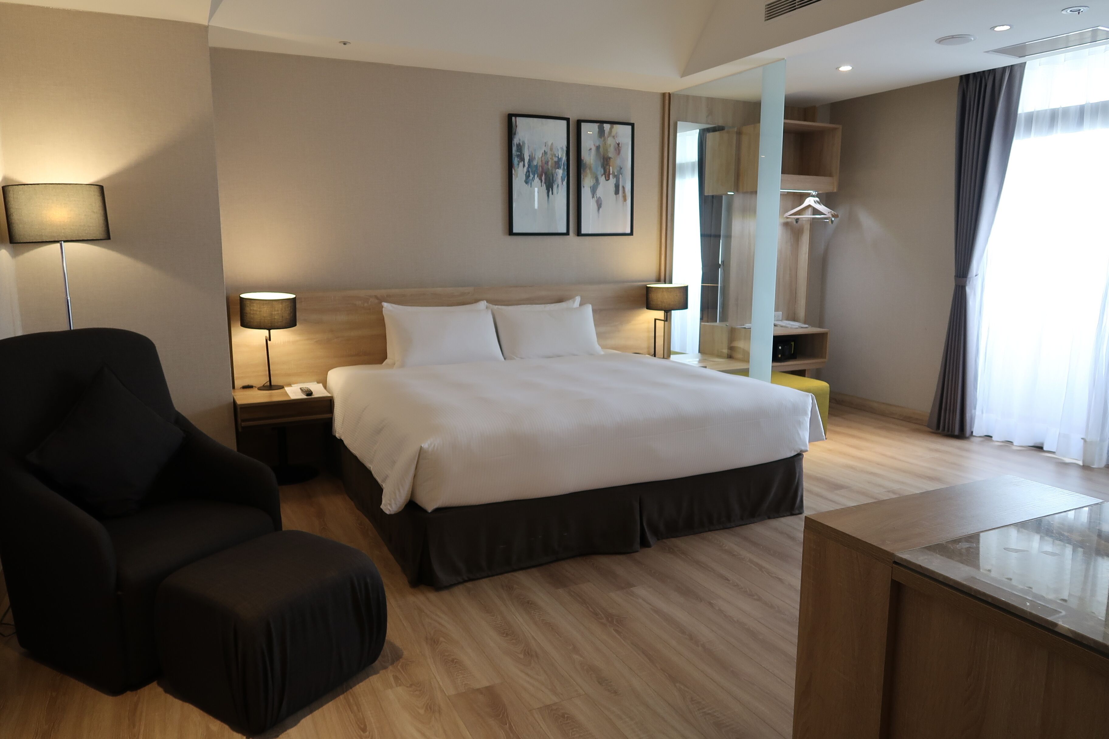 A modern hotel room with a large bed, a desk, a chair, and a mirror.