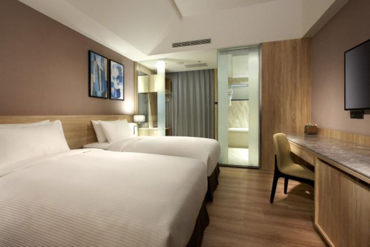 A hotel room with two beds, a desk, a chair, and a TV.
