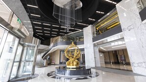 Een ruime lobby met een centraal geplaatste gouden sculptuur, een moderne kroonluchter en een marmeren vloer.
