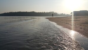 Una playa con aguas tranquilas y una persona caminando por la orilla.