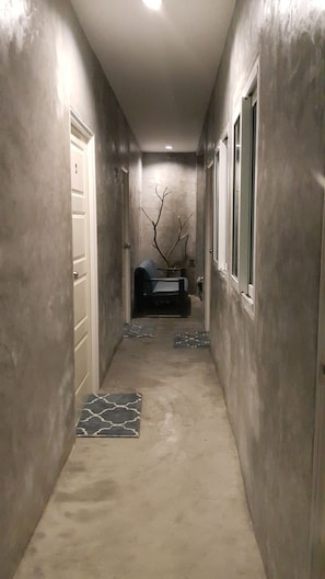 A narrow hallway with a concrete floor, a door on the left, a window on the right, and a chair in the center.