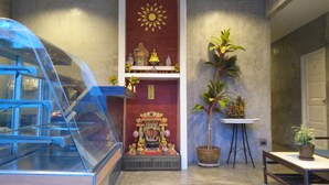Una habitación con una vitrina de vidrio, un altar rojo con un sol dorado y una planta en maceta.