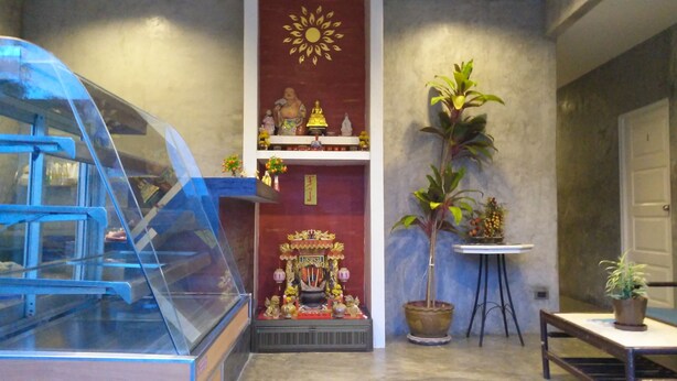 A room with a glass display case, a red altar with a golden sun, and a potted plant. - La Chambre at Lanta (Ko Lanta)