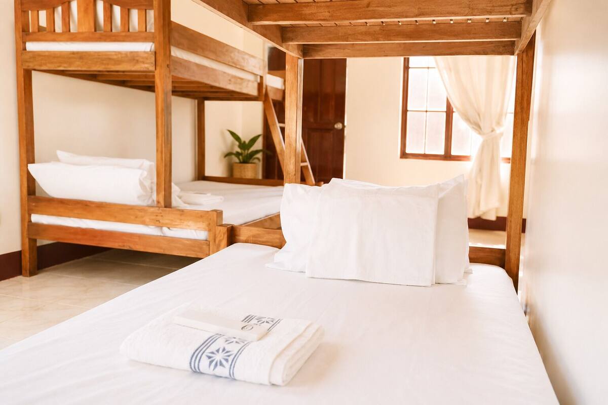 Ein Zimmer mit zwei Holzkataklanten, einem großen Bett mit weißer Bettwäsche, einer Topfpflanze und einem Fenster mit Vorhängen.