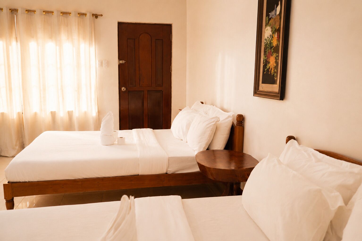A hotel room with two beds, a wooden headboard, a bedside table, a door, and a framed picture on the wall.