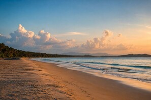 Una playa con un bote, palmeras y una cadena montañosa en la distancia.