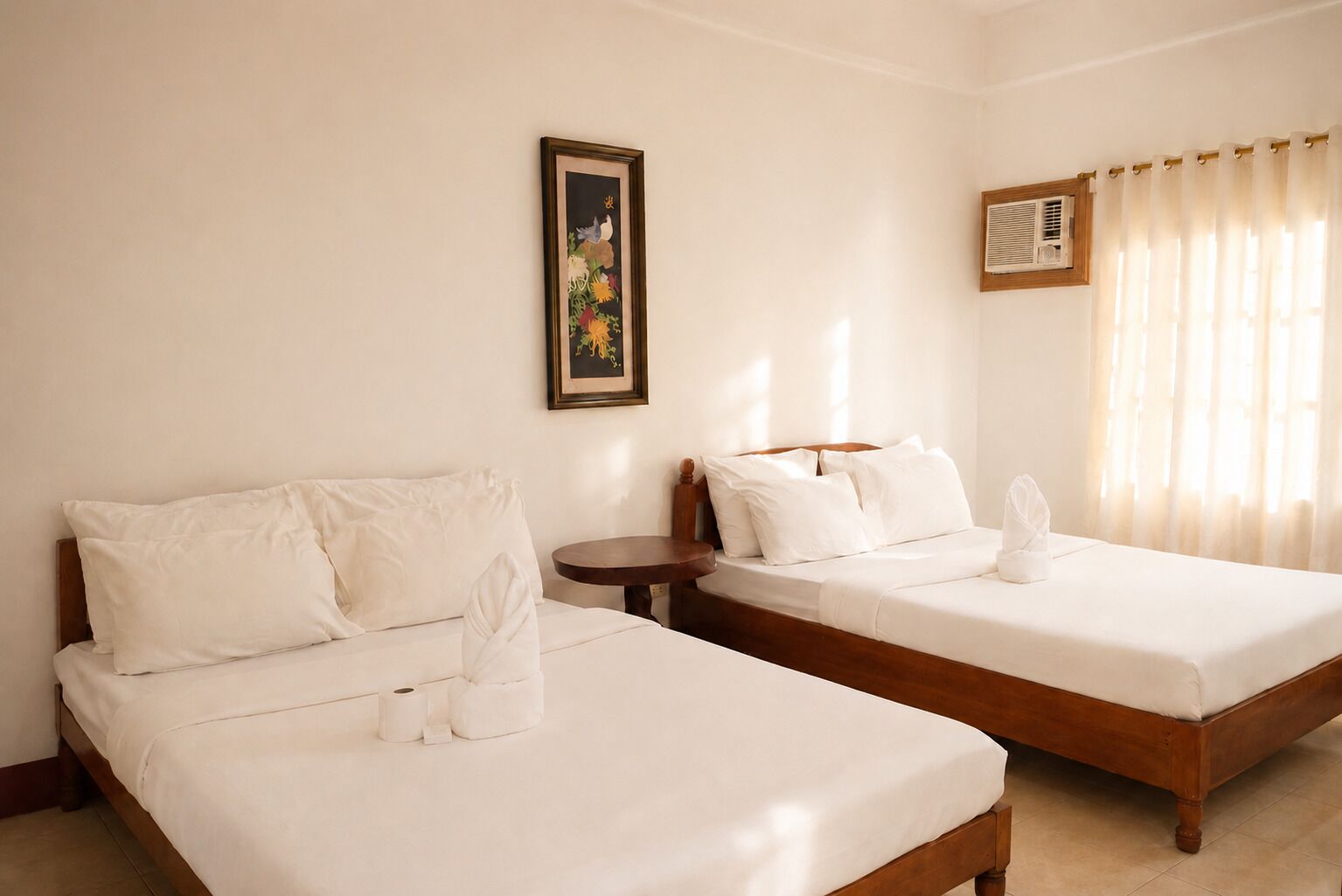 Een hotelkamer met twee bedden, een kleine ronde tafel, een lijst met een afbeelding aan de muur, en een raam met gordijnen.