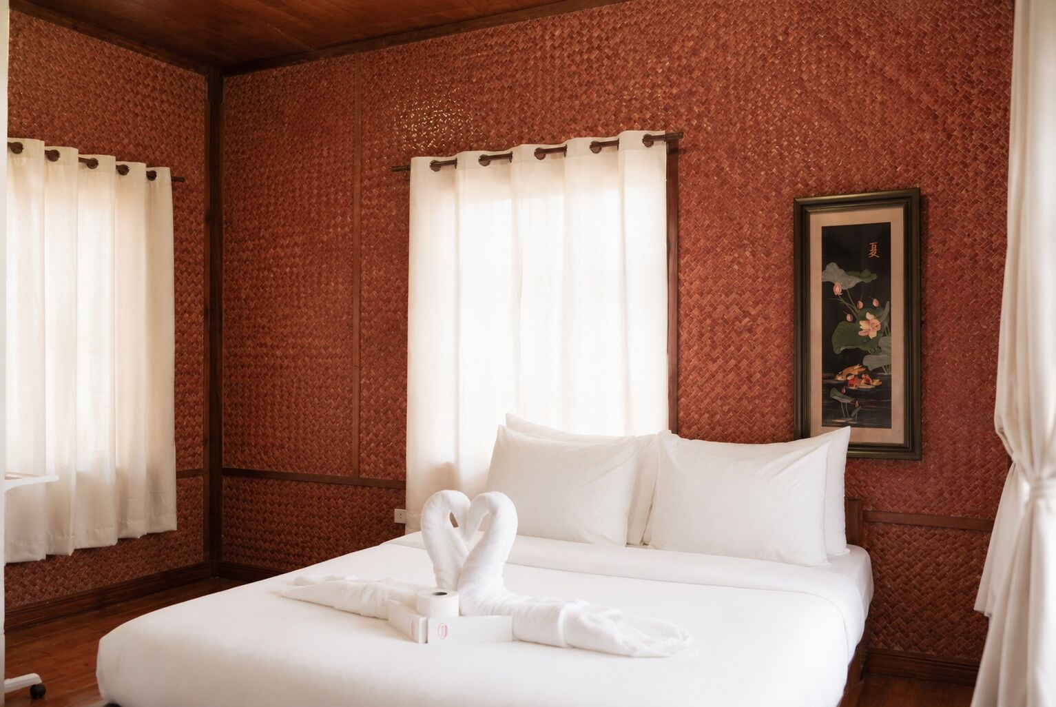 A hotel room with a large bed, white linens, a painting of lotus flowers, and a wooden ceiling.